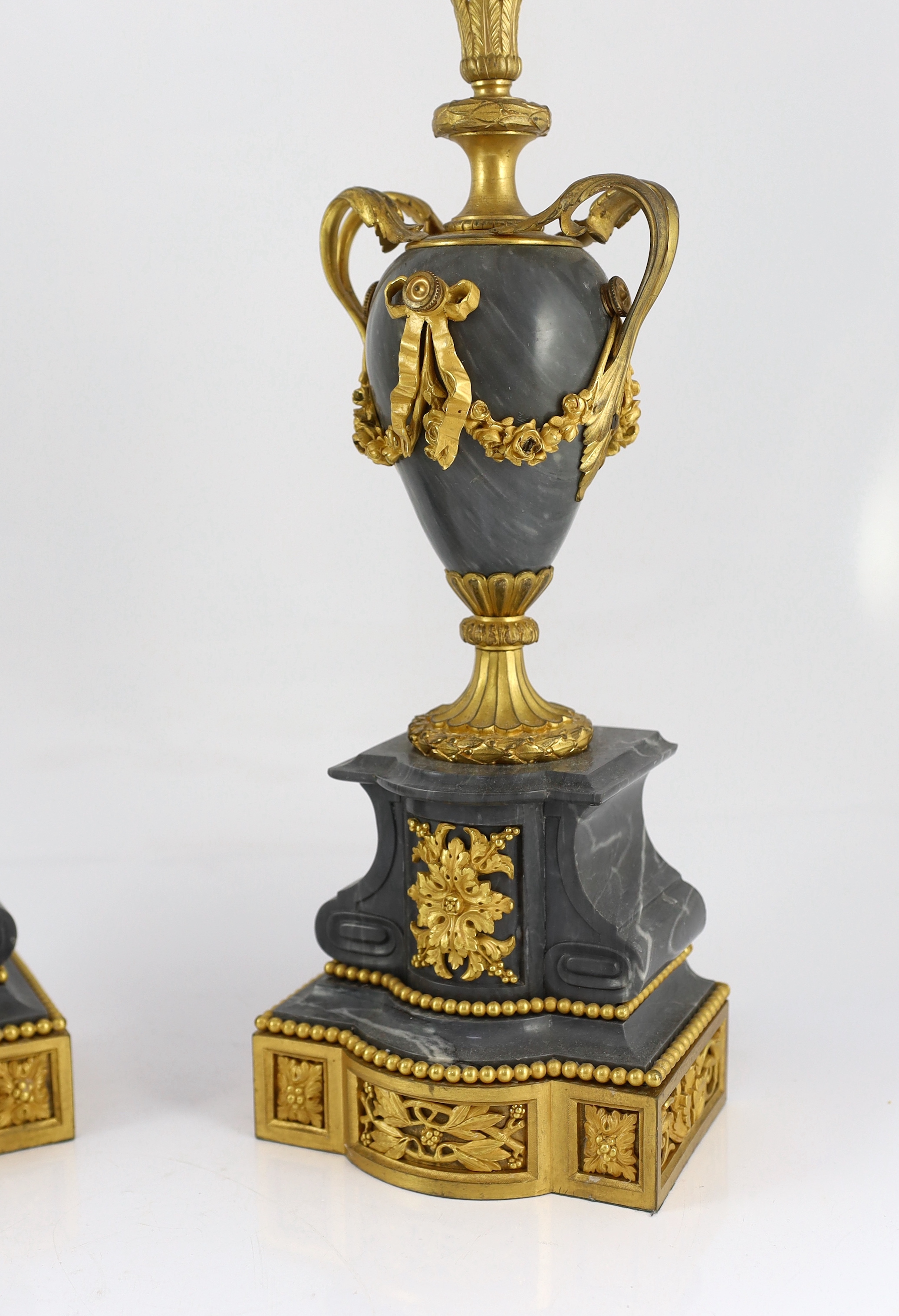 A pair of Louis XVI style ormolu and grey marble five light candelabra, with scrolling branches and urn shaped stems on architectural plinths, 26cm wide, 63cm high